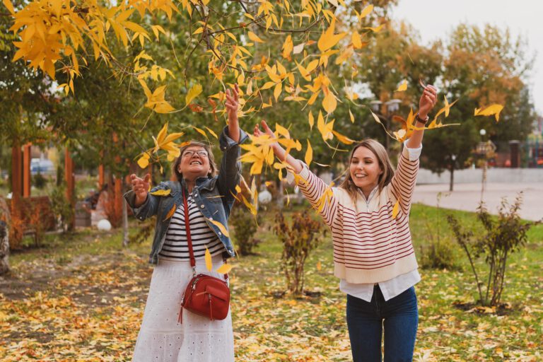 adorable women , mom and daughter are walking in a beautiful autumn park and have fun throwing autum