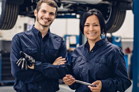 Auto car repair service center. Two happy mechanics - man and woman standing by the car